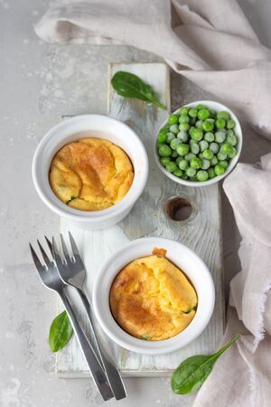 Green peas and cheese souffle in a white ceramic ramekin on light wooden board. Classic french meal.の写真素材