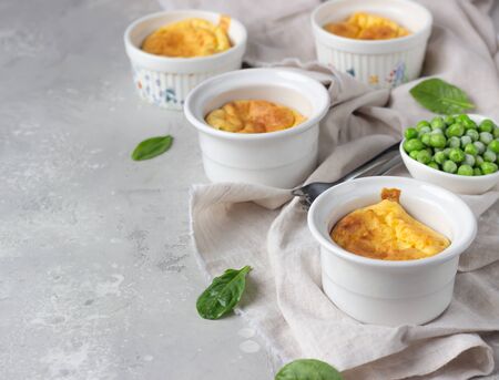 Cheese souffle with green peas in a white ceramic ramekin on a gray linen napkin. Light gray concrete background.の写真素材