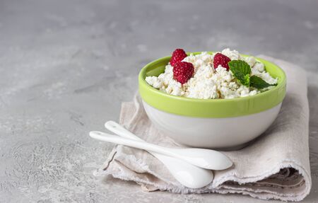 Homemade cottage cheese with raspberry and mint in a bowl. Russian homemade cottage cheese. Light gray concrete background.の写真素材