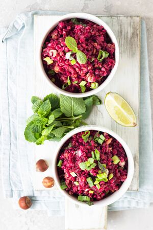 White ceramic bowls with warm buckwheat, beetroot, nuts and herbs salad on wooden board, light gray concrete background. Dietary balanced food. Vegetarian and vegan concept.の写真素材