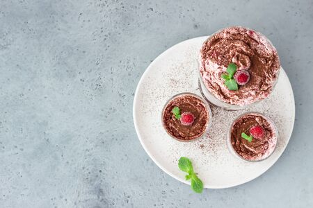 Pink layered dessert trifle, tiramisu or parfait with raspberries and mint decorated with cocoa...