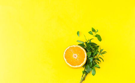 A half of orange and leaves. Creative summer concept. Food concept. Yellow background. Flat lay.