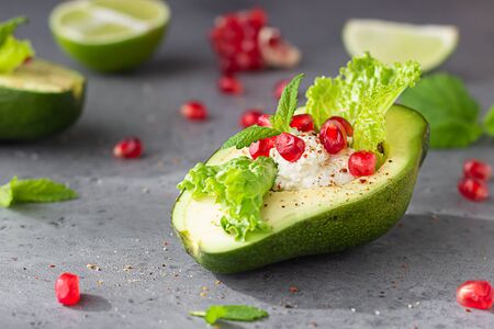 Halved avocado with cream cheese, pomegranate seeds, lettuce, mint and lime on grey stone background. Healthy food concept.の写真素材