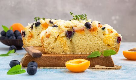 Blueberry and apricot crumble cake decorated with thyme on wooden board. Blue stone background.