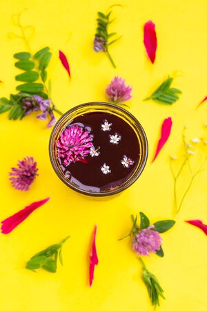 Glass with hibiscus or karkade tea with different wildflowers on yellow background.の写真素材