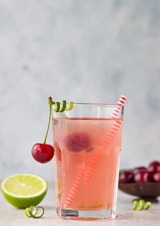 Lemonade or non-alcohol cocktail with cherry and lime in glass on gray background. Summer berry...