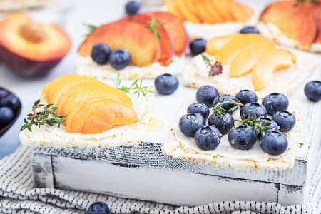 Mini sandwiches with cream cheese, fruits and berries. Healthy toasts with cream cheese, blueberries, apricots, nectarines and honey on a light blue background.の写真素材