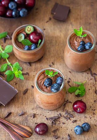 Portion jars with chocolate mousse or pudding decorated with sweet cherry, blueberry and mint and...