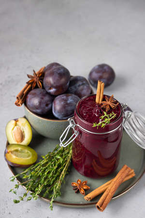 Sweet homemade spicy plum jam, fruits, thyme and spices on a gray stone table.