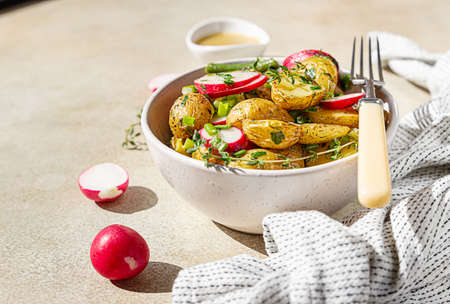 Tasty hot potato salad with green beans, fresh radishes and herbs dressing with olive oil and mustard sauce, light concrete background.の写真素材