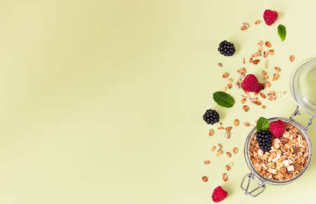 Flat lay composition with muesli or granola in jar with raspberries, blackberries and mint on pastel green background. Healthy food concept. Top view. Copy space.の写真素材