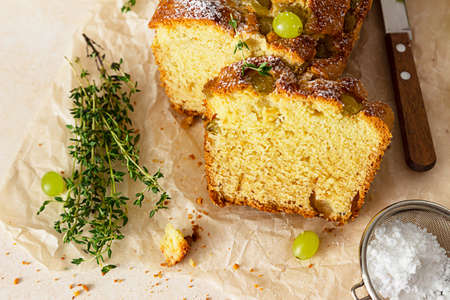 Delicious homemade grape loaf cake with thyme and sugar powder on parchment paper. Light background.