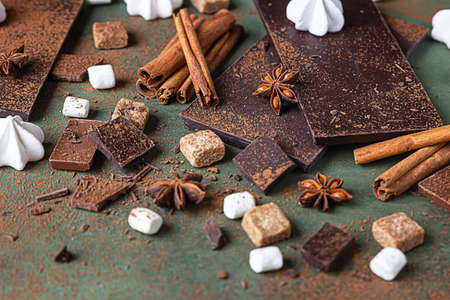 Ingredients for making hot chocolate. Dark and milk chocolate, cocoa powder, cinnamon, anise star, brown sugar, marshmallow, meringue and milk.の写真素材