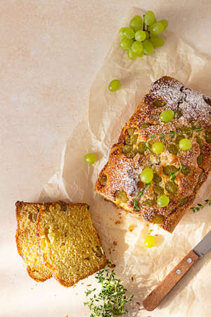 Delicious homemade grape loaf cake with thyme and sugar powder on parchment paper. Light stone...