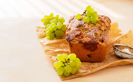 Delicious homemade grape loaf cake with thyme and sugar powder on parchment paper. Light stone background. Selective focus.の写真素材