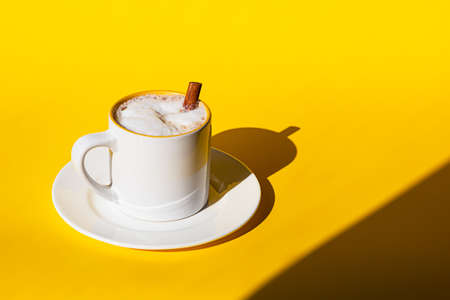 White ceramic cup of coffee or cappuccino with cinnamon on yellow background. Bright sunlight and harsh shadows.の写真素材