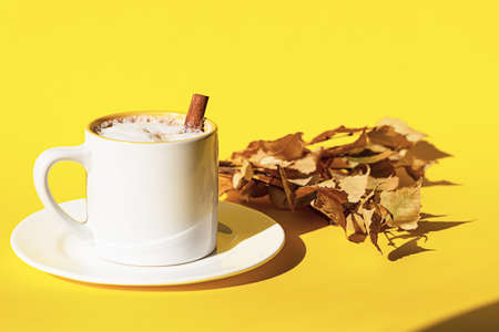 Autumn coffee or cappuccino composition. White coffee cup with milk foam, cinnamon stick and autumn...