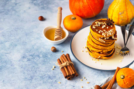Fluffy spicy pumpkin pancakes with honey and nuts, fresh pumpkins and spices on blue background.の写真素材