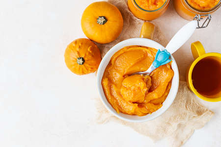Homemade pumpkin puree in bowl with baby spoon and fresh pumpkins on light concrete background. The concept of baby food.の写真素材