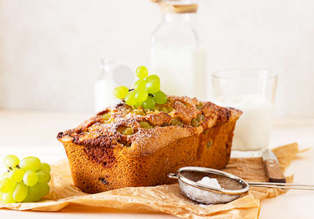 Delicious homemade grape loaf cake with thyme and sugar powder on parchment paper. Light background.
