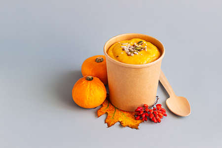 Thick vegan pumpkin cream soup with seeds in disposable cup of craft paper. Soup to go, healthy food delivery. Take away food.の写真素材