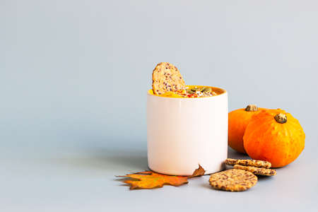 Pumpkin cream soup with seeds and cream in ceramic mug and multigrain healthy crackers on blue background.の写真素材