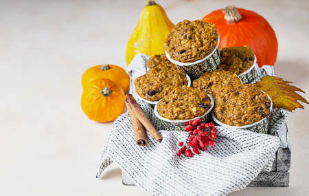 Wooden tray with vegan pumpkin muffins, cinnamon and fresh pumpkins on light background. Autumn of winter baking.の写真素材