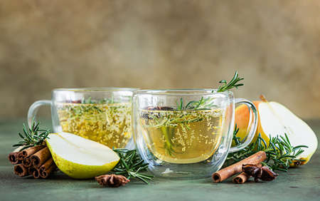 Spicy hot pear or apple cider with cinnamon, anise and rosemary. Traditional autumn or winter drinks. Green concrete background. Selective focus.の写真素材