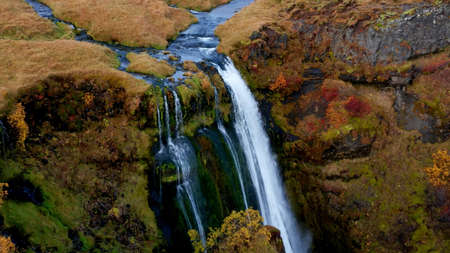Aerial view of a waterfall in the middle of a canyon in autumn
