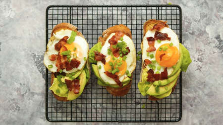 Top view of toasts with avocado, fried egg and bacon on gray background