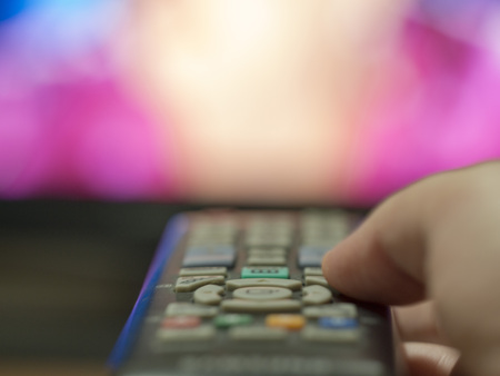 Remote control. girl changes television channel by pressing with a finger the remote control button pointed on tv blurry in the backgroundの写真素材