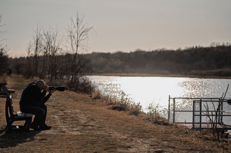 Man with a camera on the bank of a lake at sunset.の写真素材