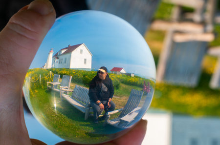 Crystal ball reflecting a man sitting on bench in front of a houseの写真素材