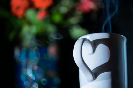 steaming cup of coffee and a bouquet of red flowers in backgroundの写真素材