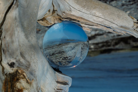 crystal ball on driftwood reflecting the beach and the riverの写真素材