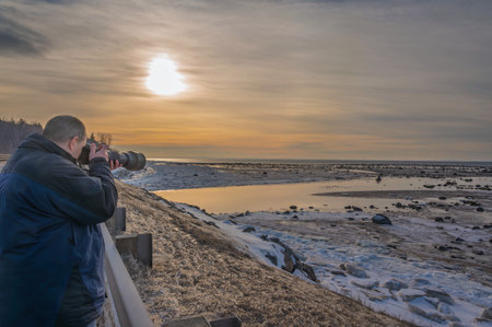 a man takes photos of the rising sun on the side of the road along the coastの写真素材