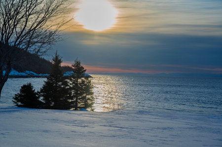 Beautiful winter landscape with frozen lake and snow covered trees at sunsetの写真素材