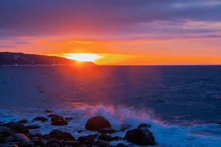 Sunset over the sea with waves crashing on the rocks and rocky shoreの写真素材