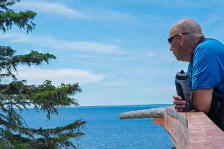 A man in a blue T-shirt with a camera looks at the sea.の写真素材
