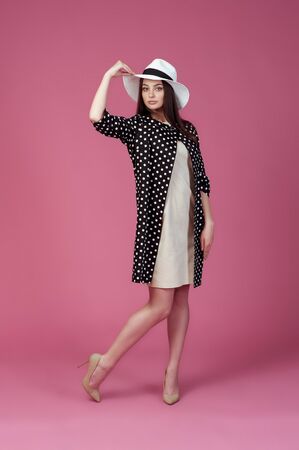 Beautiful young woman in elegant beige dress, polka dot jacket and summer hat. Girl posing on a pink background. Fashion photo.の写真素材