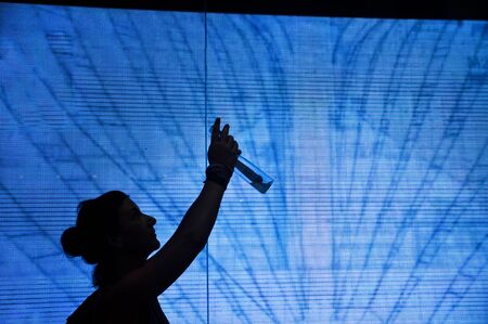 A silhouette of a woman standing in front of a wall of screens take a picture with smartphone.