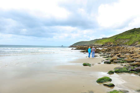 Portholland, Cornwall / UK - July 05, 2020: Two people walking on the beach in Porthluney Bay with...