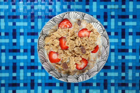 Close-up of corn flakes and milk with strawberry in a bowl viewed from above, isolated on white blue...