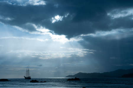 Dramatic sky with clouds and sunbeam over the Indian Ocean with sailing boat during sunset.