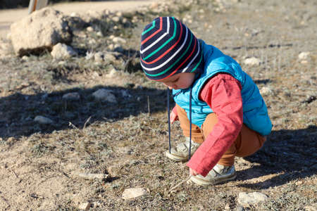 Toddler boy playing with wooden stick and rock on a field. Nature connection.の写真素材