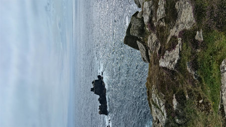 A scenic view of rocky cliffs and the ocean under a cloudy sky, capturing the rugged coastline of...