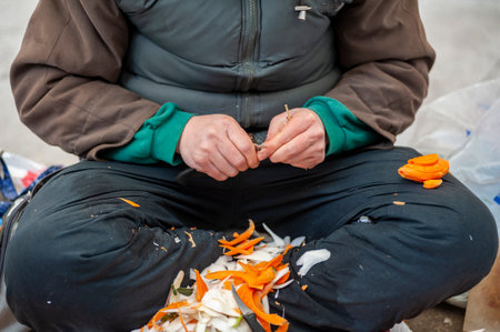 A man in a green jacket is sitting on the street and making a vegetable salad.の写真素材