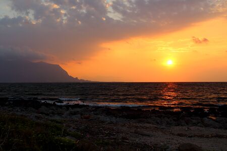 evocative image of sunset over the sea with promontory in the backgroundの写真素材