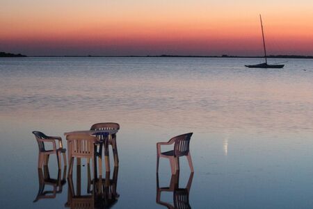 tables and chairs by the sea at sunset and moored boats and headland in the backgroundの写真素材