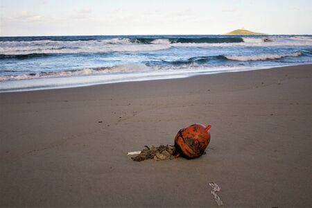 evocative closeup image of abandoned buoy on sandy beach with rough seas and small island in the backgroundの写真素材